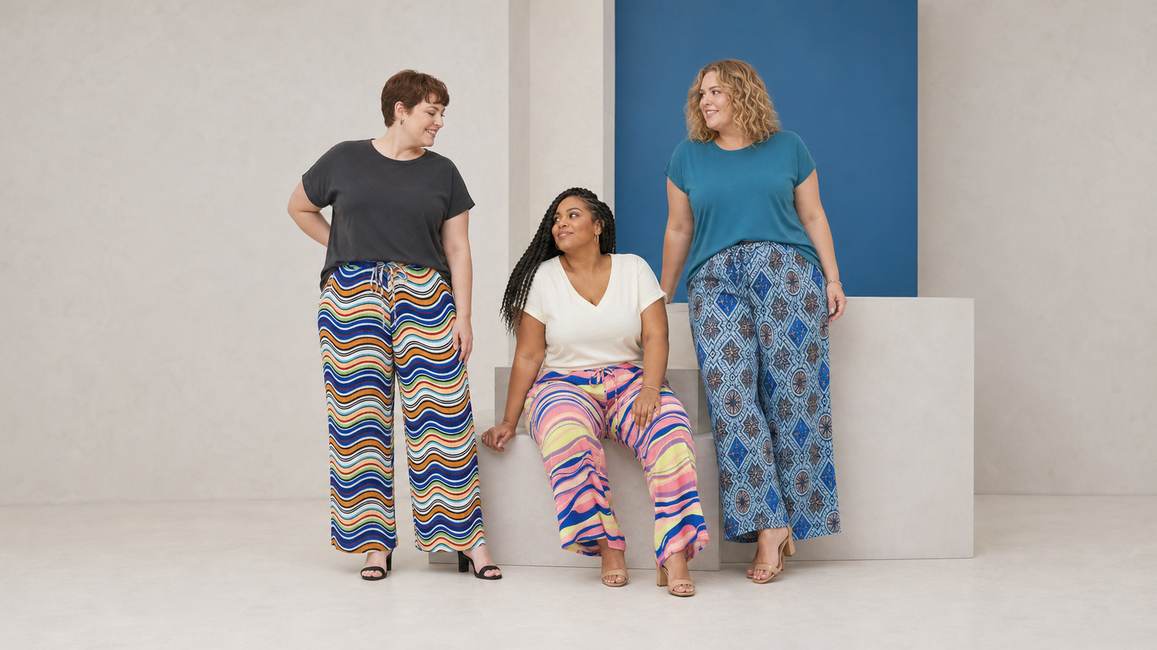Three plus-size women wearing colourful pleated wide-leg trousers featuring wavy stripes, abstract prints and blue geometric patterns with simple tops.