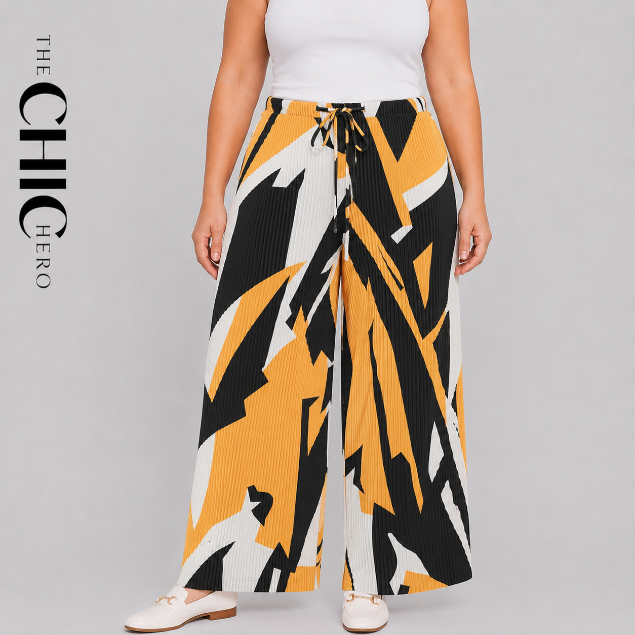 A model wearing wide-leg pleated trousers with an abstract geometric pattern in yellow, black, and white. The pants feature a drawstring waist and are styled with a white top and white flat shoes against a solid gray background.