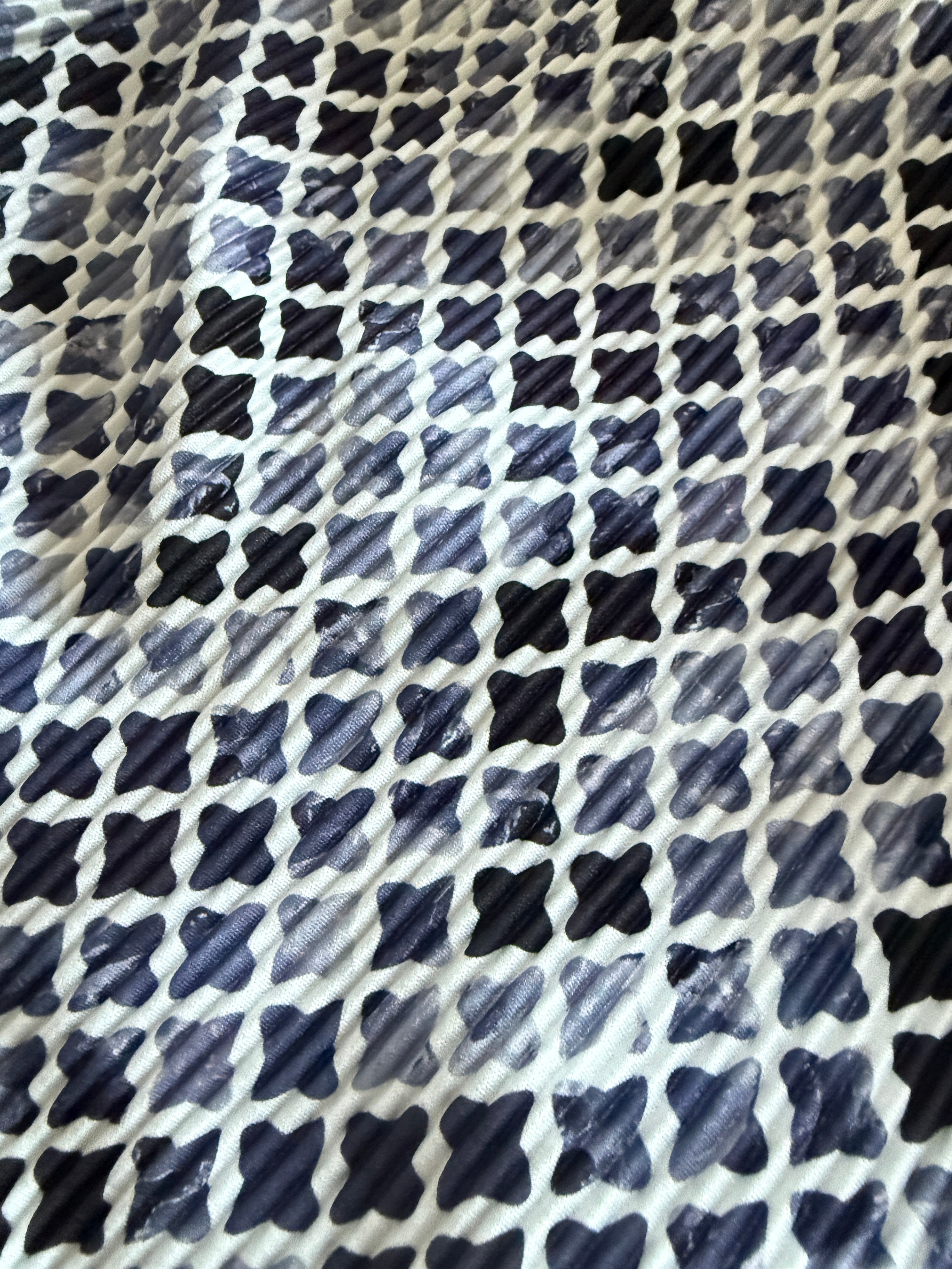A close-up of a fabric or material surface with a repeating geometric pattern of dark navy and black brushstroke-style shapes on a white background.