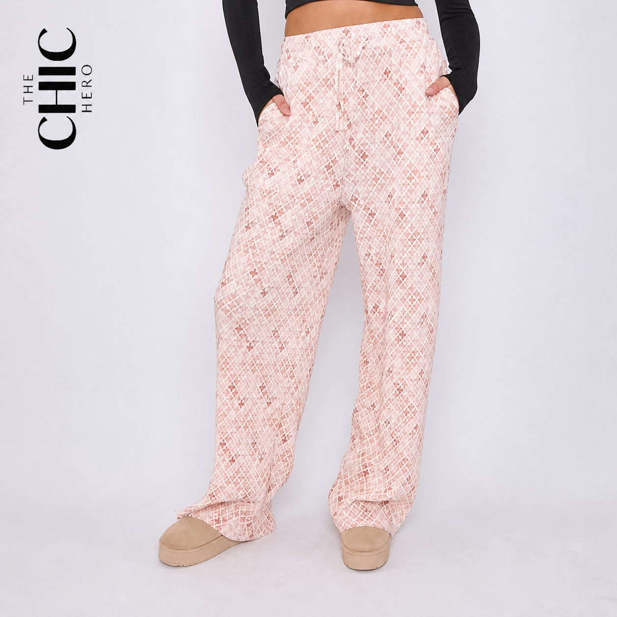 A model wearing light pink wide-leg pants with a white geometric pattern, styled with a black long-sleeve crop top and beige slip-on shoes. The brand logo 'THE CHIC HERO' is visible in the top left corner.