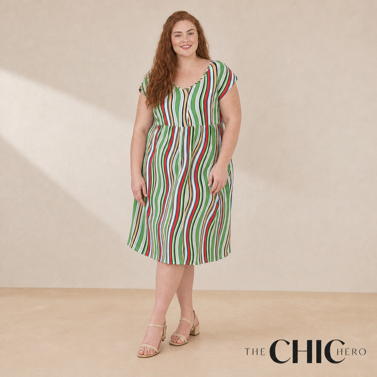 A woman modeling a sleeveless midi dress with vertical green, red, and white stripes, standing against a beige studio backdrop. The brand logo 'THE CHIC HERO' is visible in the bottom right corner.