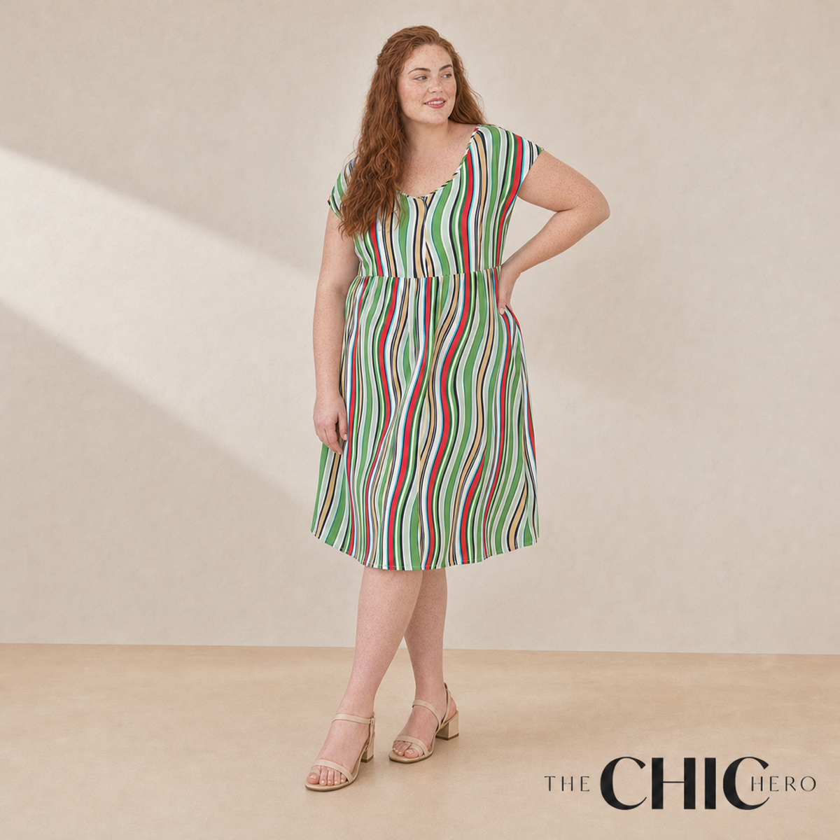 A woman modeling a sleeveless midi dress with vertical green, red, and white stripes, standing against a beige studio backdrop. The brand logo 'THE CHIC HERO' is visible in the bottom right corner.