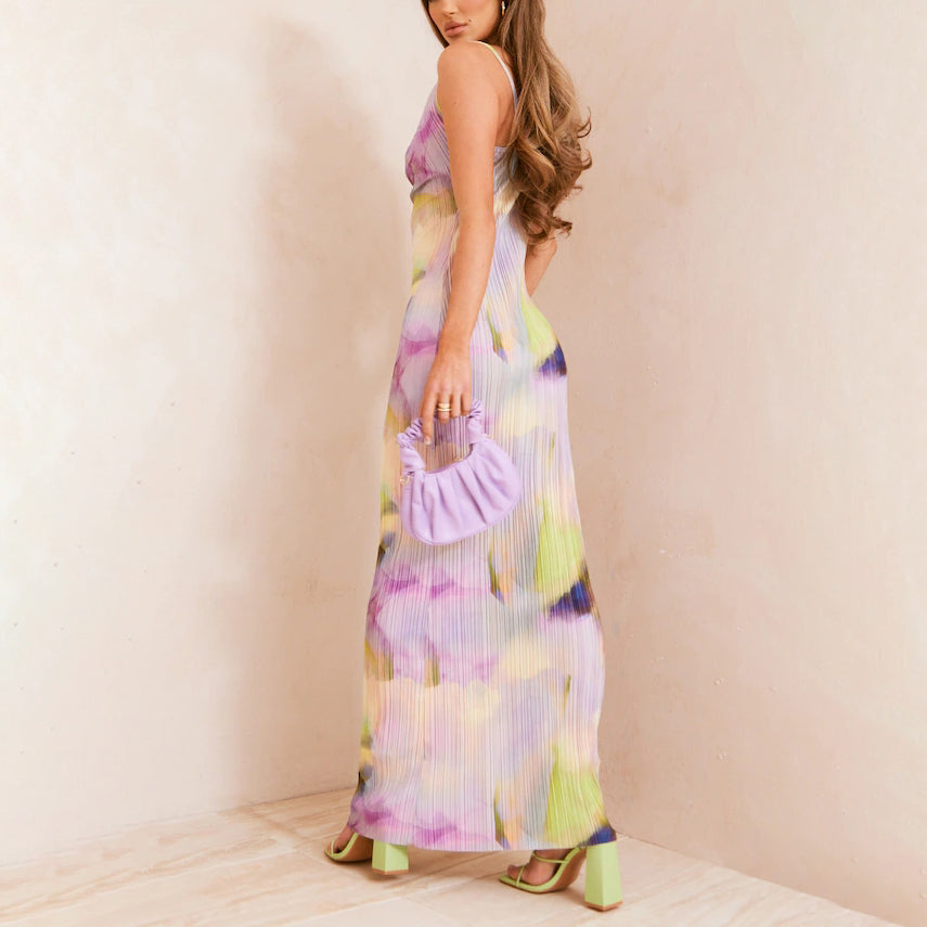 Woman in a colorful dress holding a purple bag against a plain background