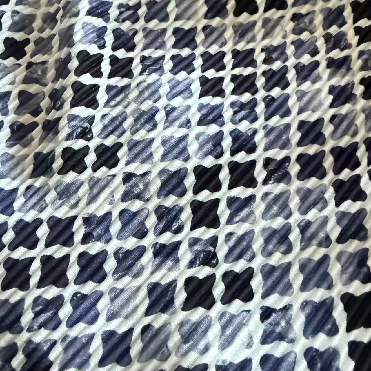 A close-up of a patterned fabric featuring a repeating grid of dark navy and black brushstroke-style crosses on a white background.
