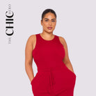 Woman wearing a red jumpsuit with 'The Chic Hero' branding on a light gray background