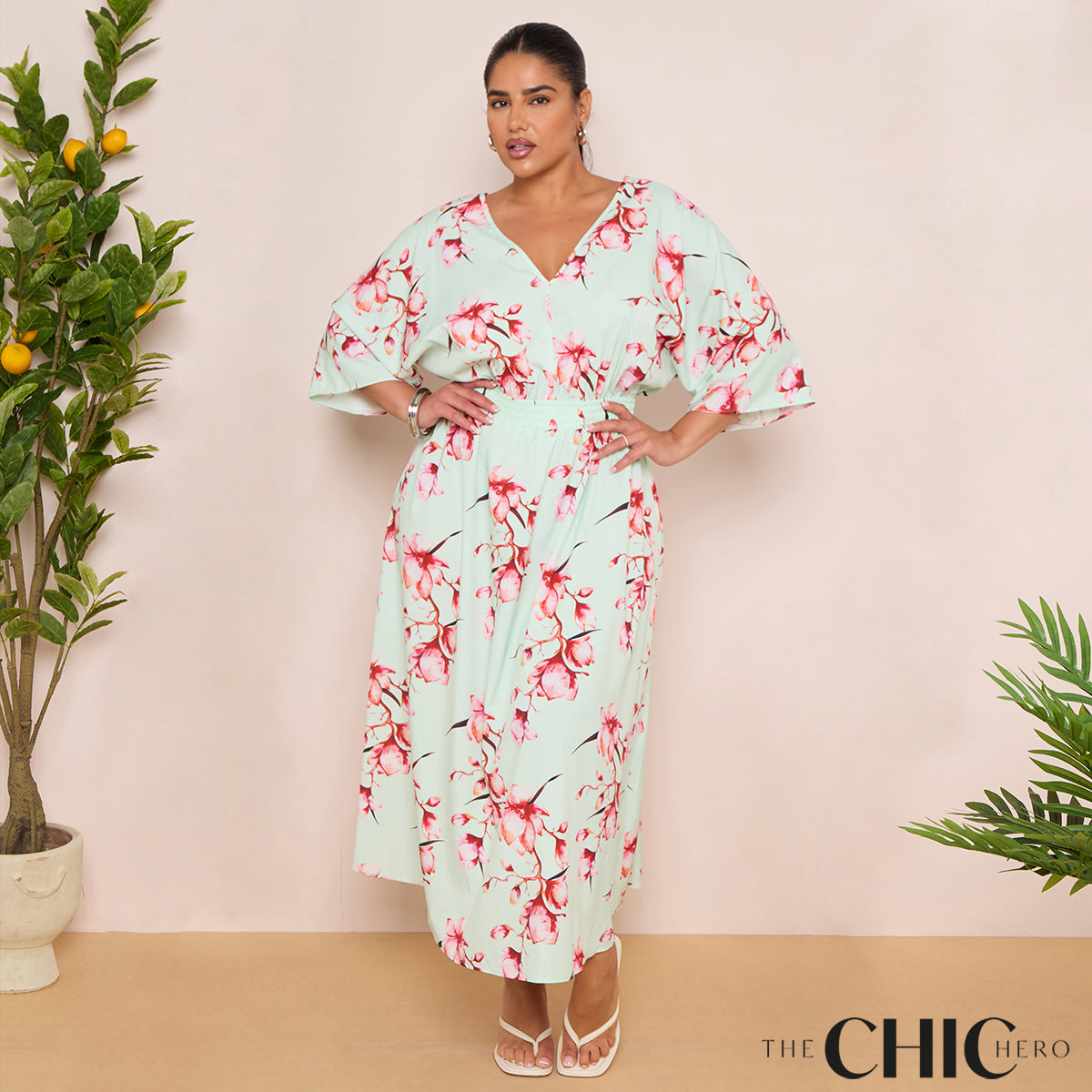 Woman wearing a floral dress with greenery on either side against a beige background, featuring 'The Chic Hero' brand.