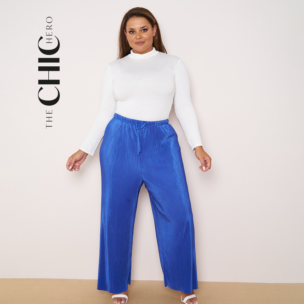 A model wearing wide-leg royal blue drawstring pants with a black tank top and black loafers, shown against a light gray studio background with 'THE CHIC HERO' text on the left.
