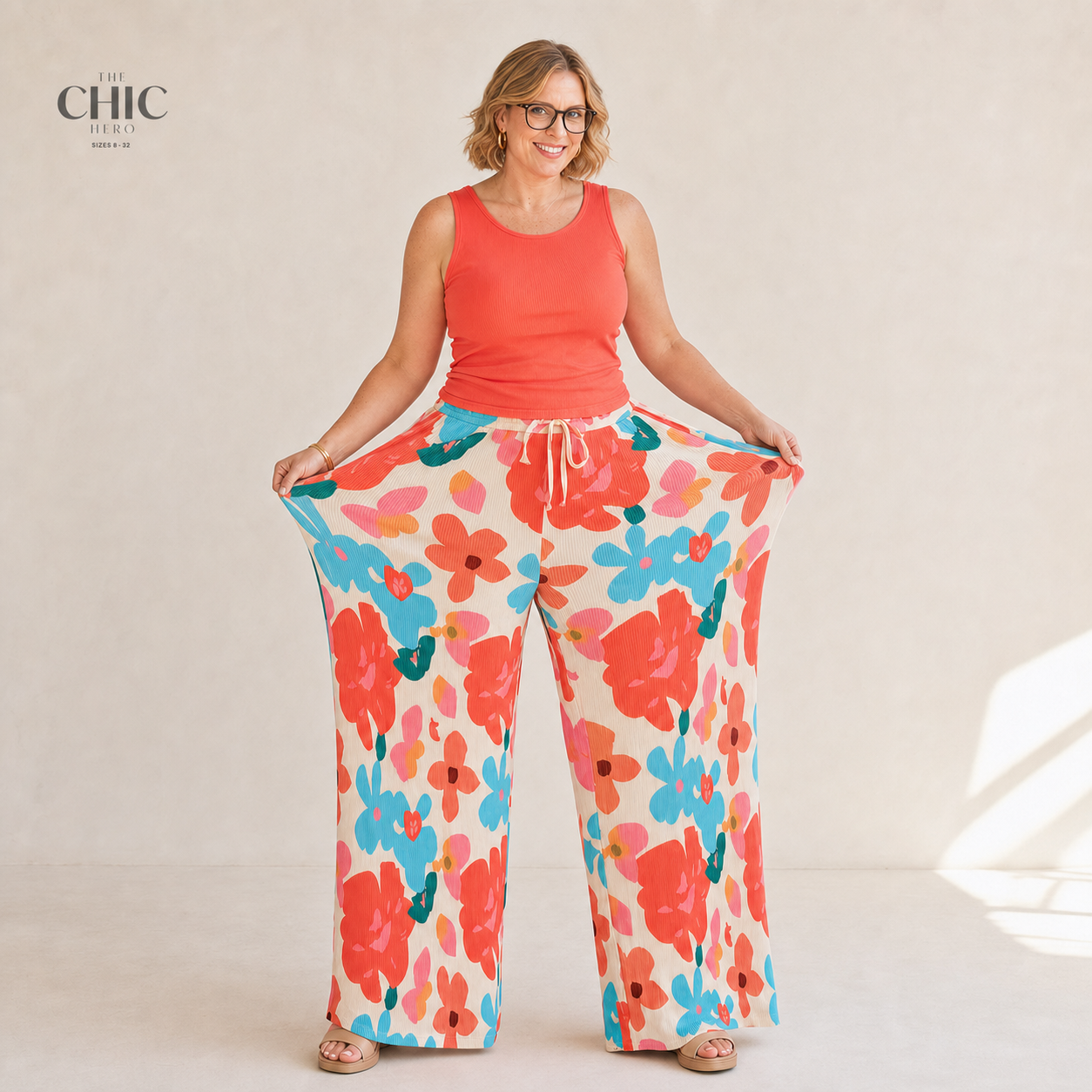 A model wearing wide-leg pants with a colorful floral print in orange, blue, and pink on an off-white background, paired with a coral orange top. The brand logo 'THE CHIC PARIS' is visible in the top left corner.