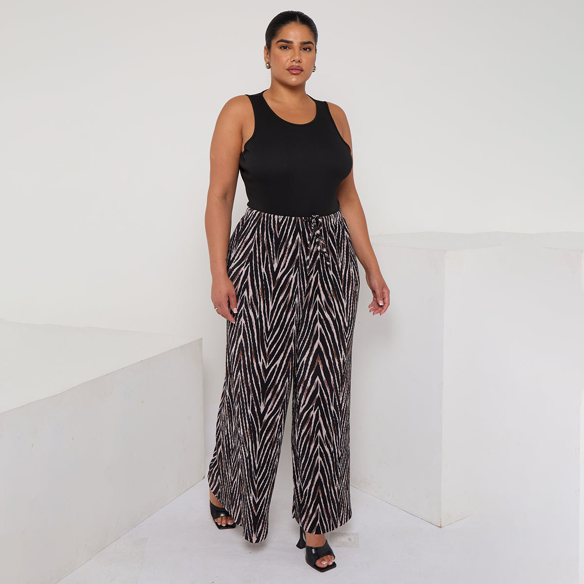 Woman wearing a black sleeveless top and patterned pants on a white background