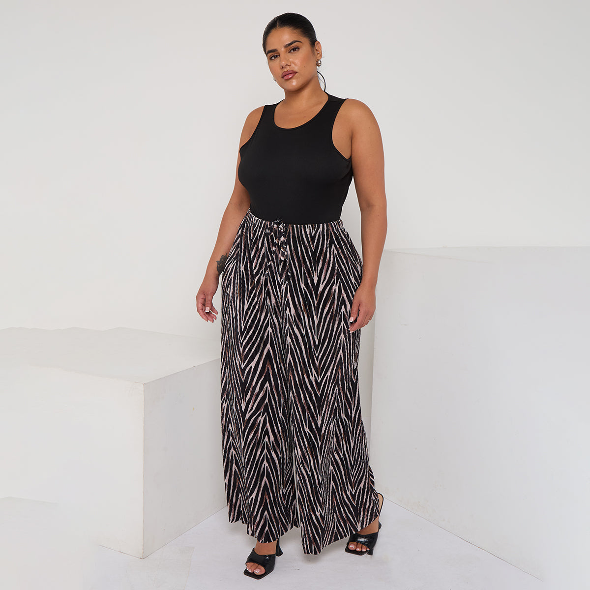 Woman wearing a black sleeveless top and patterned skirt on a white background