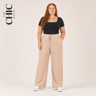 A woman modeling wide-leg beige trousers with a drawstring waist, paired with a black short-sleeve top and white sneakers, against a light beige studio background. The brand logo 'THE CHIC HERO' is visible in the top left corner.