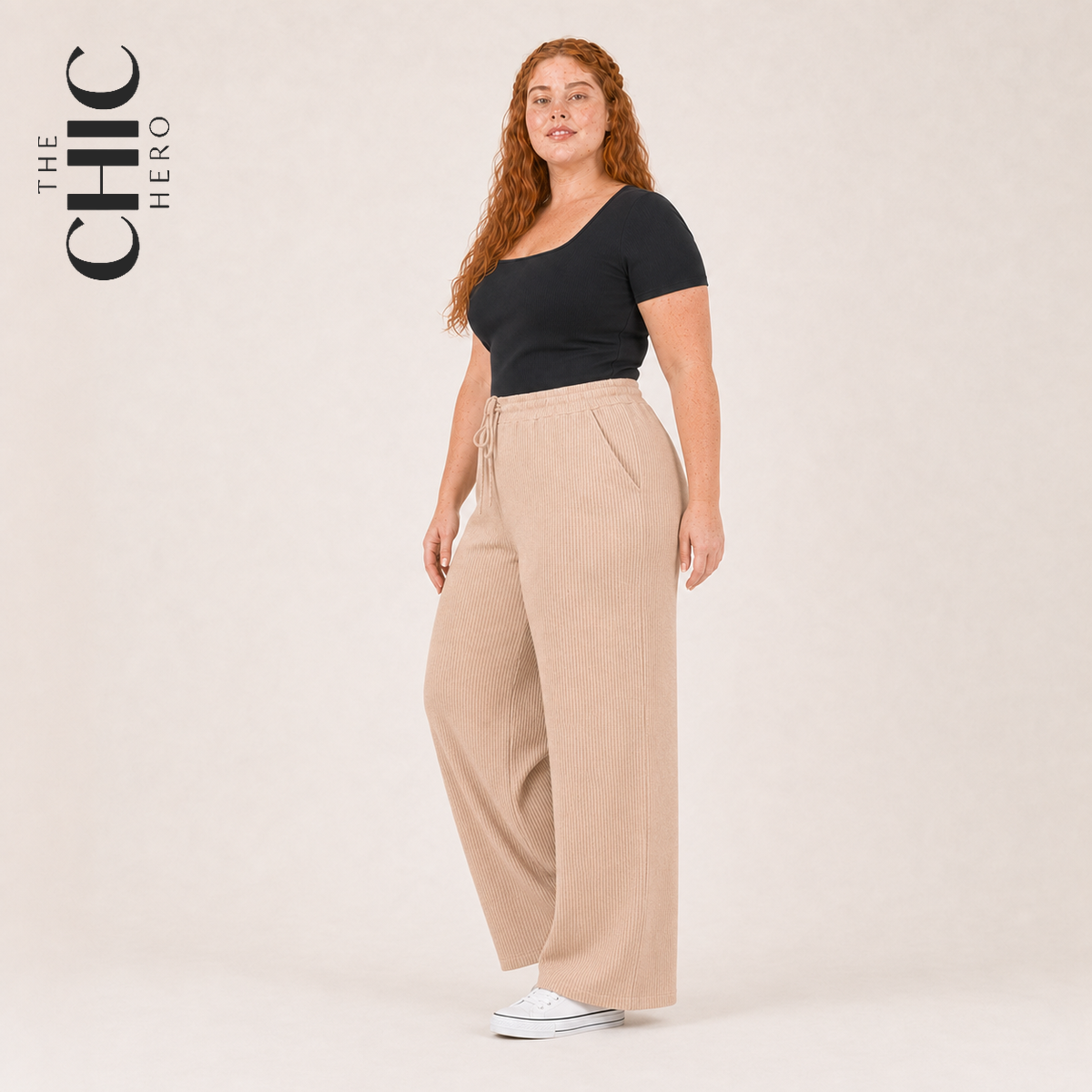 A woman modeling a black short-sleeve top and beige wide-leg pleated pants against a light beige studio background. The brand logo 'THE CHIC HERO' is visible in the top-left corner.
