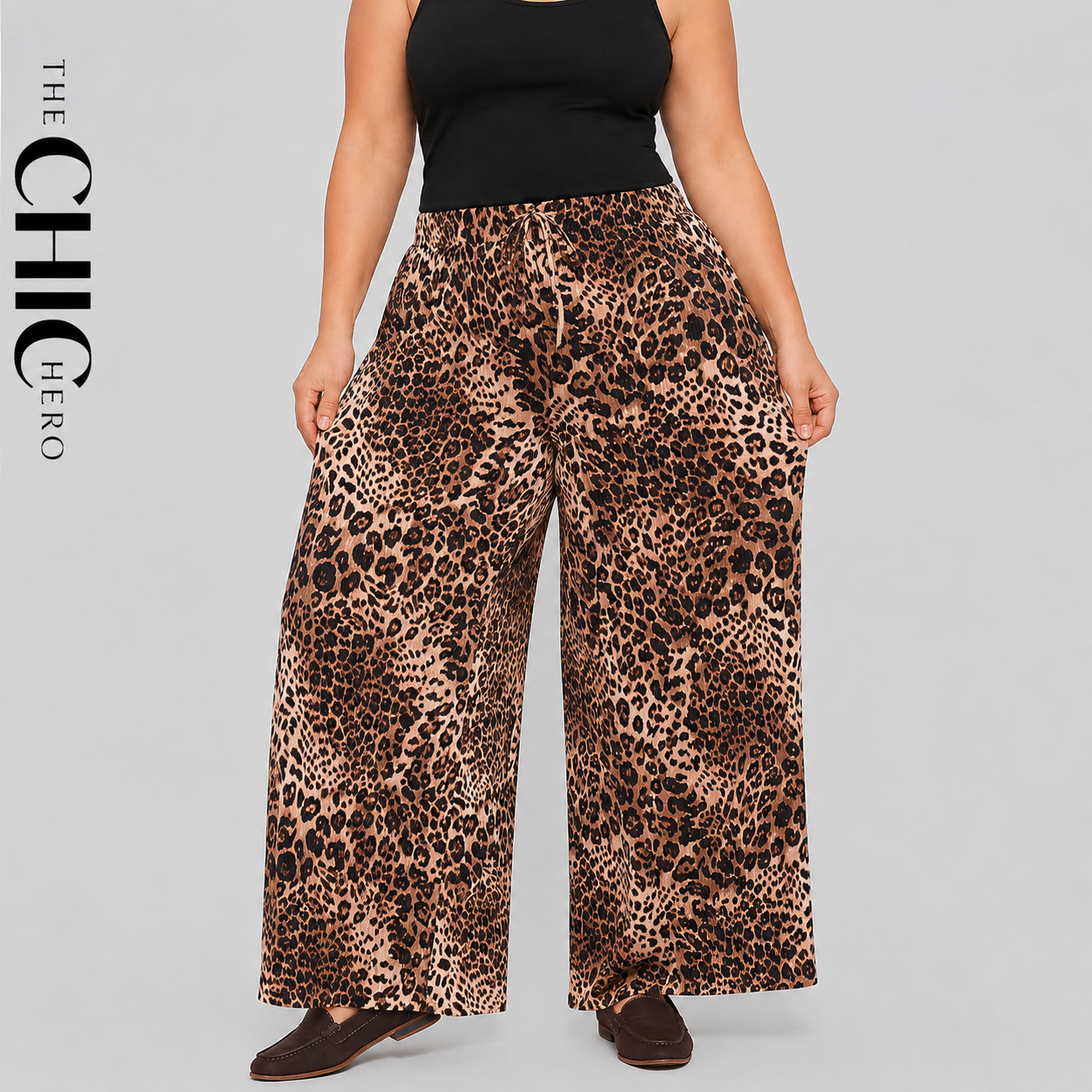A model wearing wide-leg leopard print pants with a black tank top, shown from the chest down against a light gray studio background. The brand name 'THE CHIC HERO' is printed vertically on the left side.
