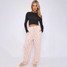 A woman modeling a black long-sleeve crop top and light pink patterned wide-leg pants against a plain white studio background.