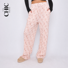 A model wearing light pink wide-leg pants with a white geometric pattern, styled with a black long-sleeve crop top and beige slip-on shoes. The brand logo 'THE CHIC HERO' is visible in the top left corner.
