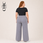 A woman shown from the back wearing a black short-sleeve top and light gray wide-leg ribbed pants, standing against a plain light beige studio background. The brand name 'THE CHIC HERO' appears in the upper left corner.