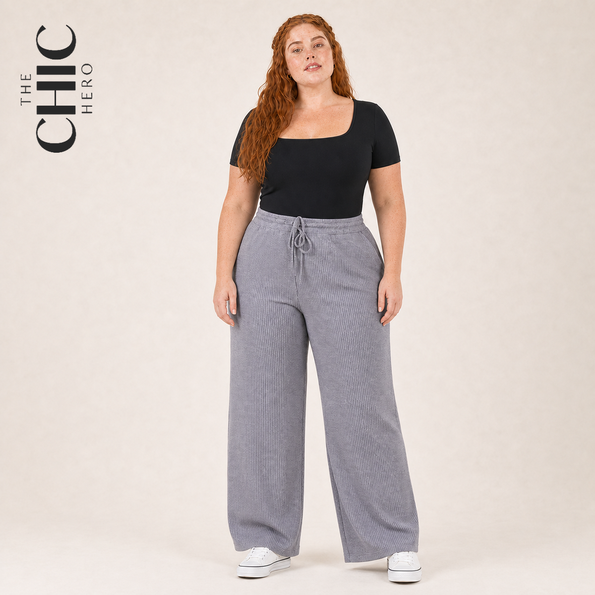 A woman modeling a black scoop-neck short-sleeve top and light gray wide-leg ribbed drawstring pants, standing against a plain beige studio background. The text 'THE CHIC HERO' appears in the upper left corner.