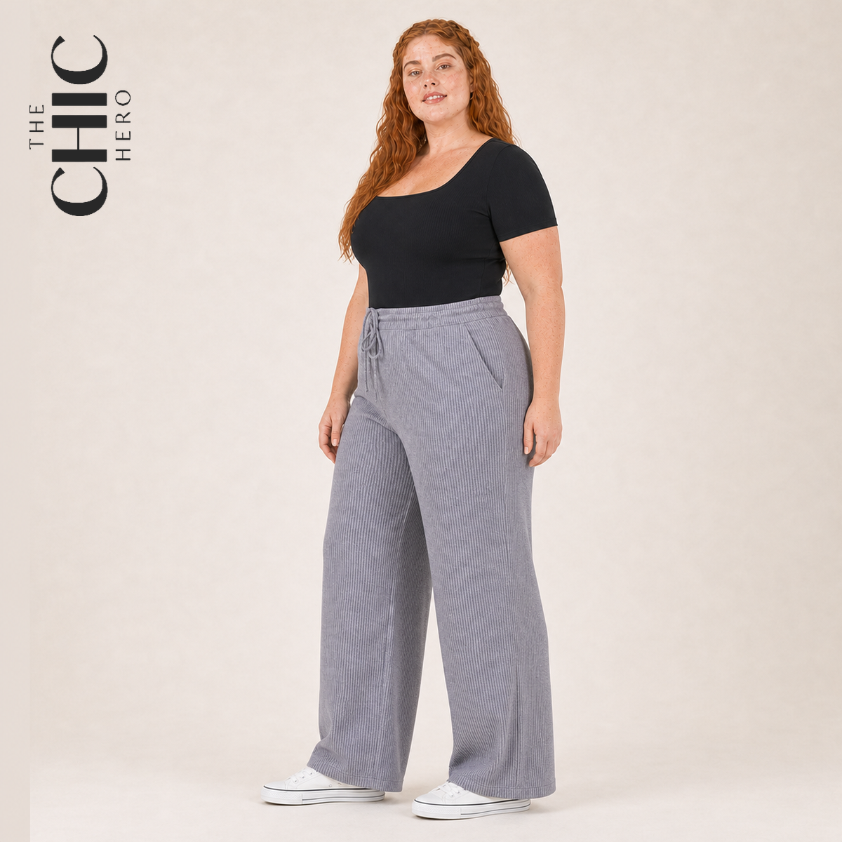 A woman modeling a black scoop-neck short-sleeve top and light gray wide-leg ribbed drawstring pants, standing against a plain beige studio background. The text 'THE CHIC HERO' appears in the upper left corner.