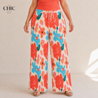 A model wearing wide-leg pants with a colorful floral print in orange, blue, and pink on an off-white background, paired with a coral orange top. The brand logo 'THE CHIC PARIS' is visible in the top left corner.