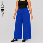 A model wearing wide-leg royal blue drawstring pants with a black tank top and black loafers, shown against a light gray studio background with 'THE CHIC HERO' text on the left.